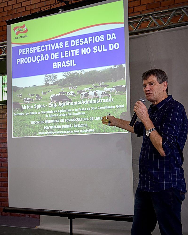 Airton Spies at the microphone in front of a slide from his talk on milk production